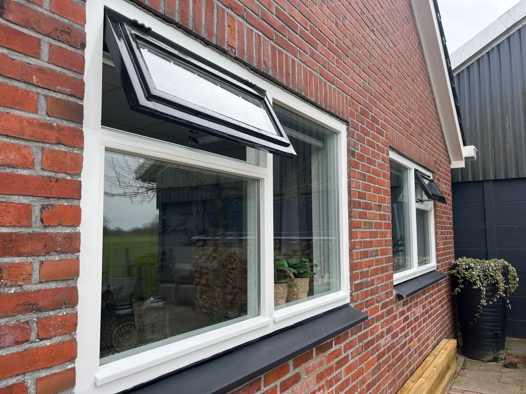 Buitenwerk: kozijnen (na) — Strak geverfde kozijnen: wit met zwarte accenten tegen de gevel. N. Boersma Schilderwerken, Drachten.